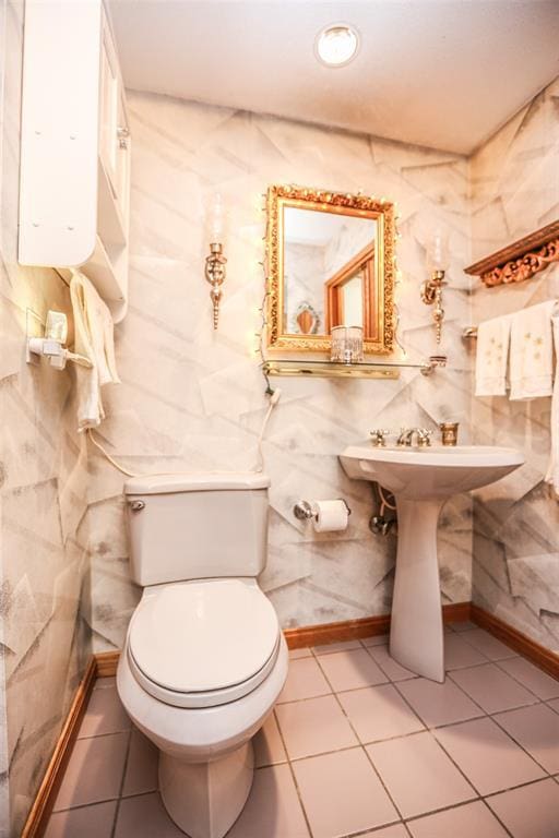 half bathroom featuring tile patterned floors, toilet, baseboards, and tile walls