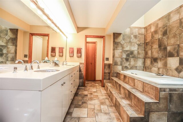full bath featuring stone finish flooring, a bath, double vanity, and tile walls