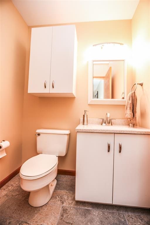 bathroom with toilet, vanity, baseboards, and stone finish flooring