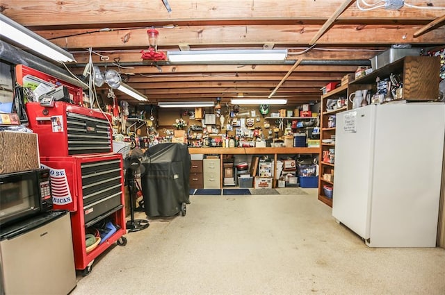 unfinished basement featuring freestanding refrigerator, a workshop area, and fridge