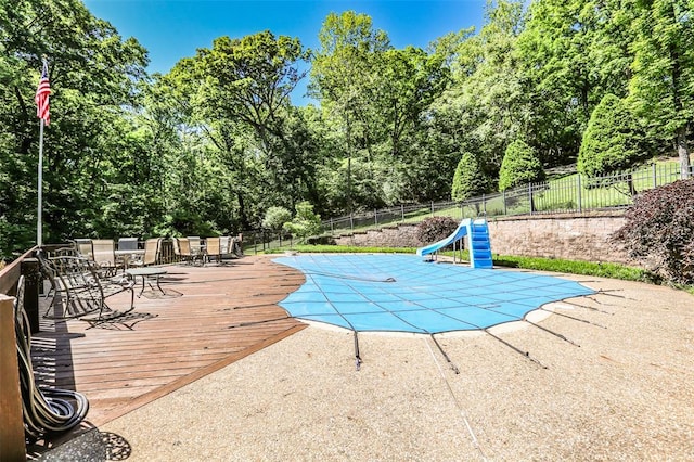 view of swimming pool with a water slide, outdoor dining space, fence, and a patio area