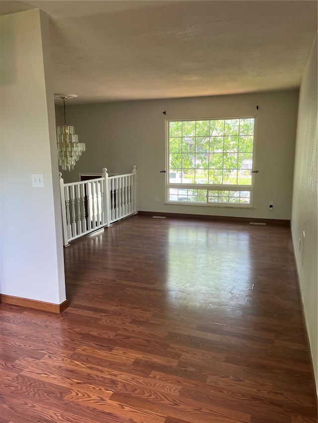 spare room featuring a chandelier, dark wood finished floors, and baseboards