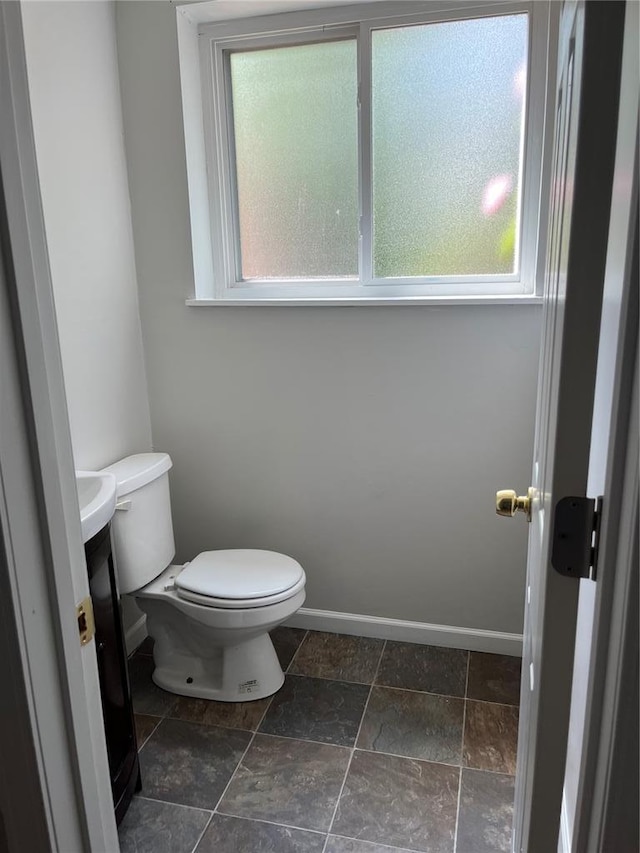 half bath with healthy amount of natural light, toilet, vanity, and baseboards