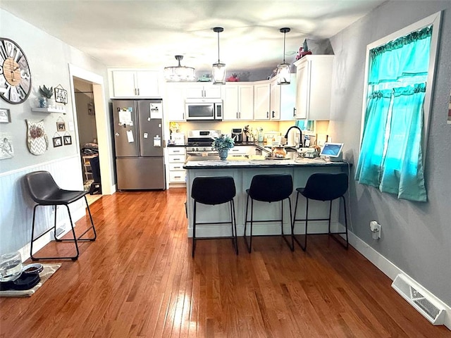 106 W Iowa St, Trenton, IL 62293 - kitchen with appliances with stainless steel finishes, a peninsula, dark wood-type flooring, white cabinets, and pendant lighting