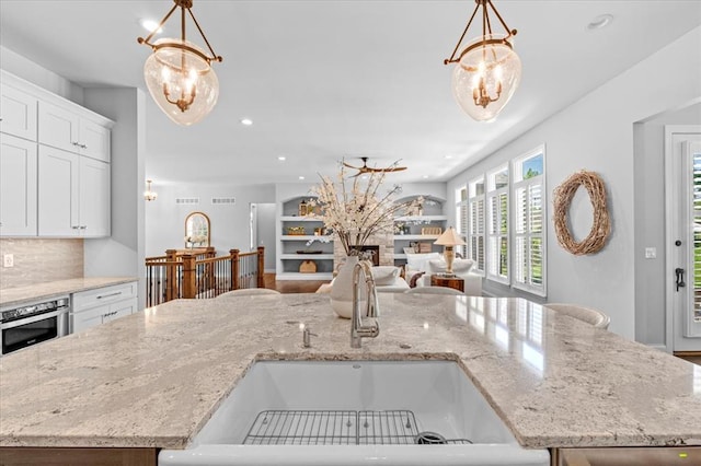 2604 Center Ave, Wildwood, MO 63040 - kitchen with a sink, hanging light fixtures, white cabinets, light stone countertops, and recessed lighting