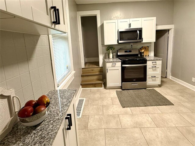 2327 Shirley Ave, Jennings, MO 63136 - kitchen featuring appliances with stainless steel finishes, light stone counters, white cabinetry, baseboards, and light tile patterned floors