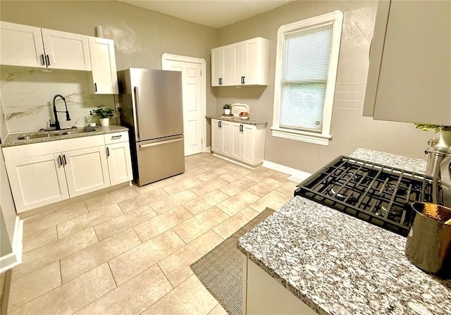 2327 Shirley Ave, Jennings, MO 63136 - kitchen featuring freestanding refrigerator, a sink, backsplash, white cabinets, and light stone counters