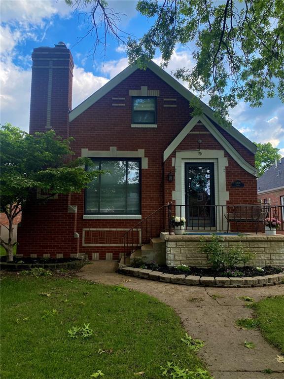 tudor home featuring brick siding, a chimney, and a front yard