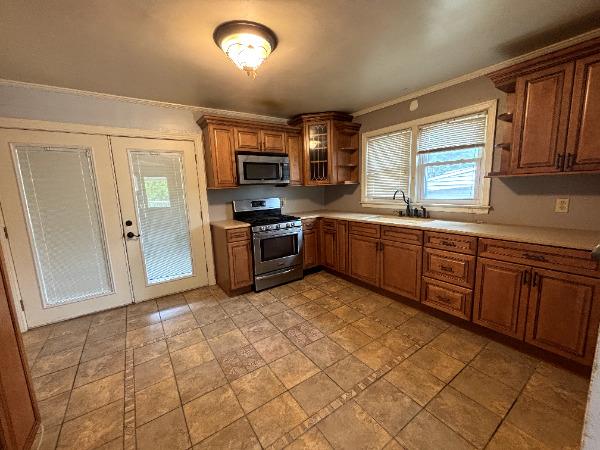 kitchen with stainless steel appliances, a sink, open shelves, light countertops, and ornamental molding