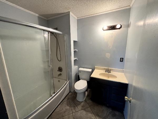 bathroom with crown molding, toilet, vanity, a textured ceiling, and bath / shower combo with glass door