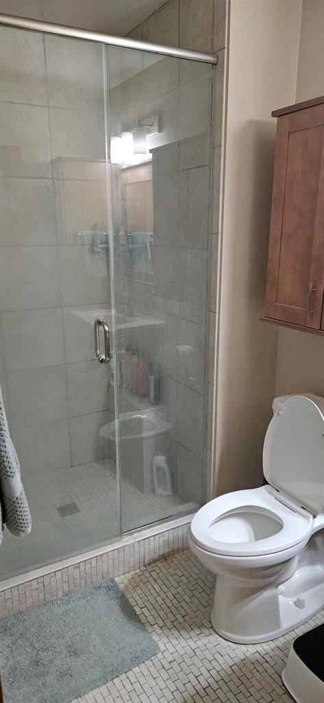 full bath with toilet, a stall shower, and tile patterned flooring