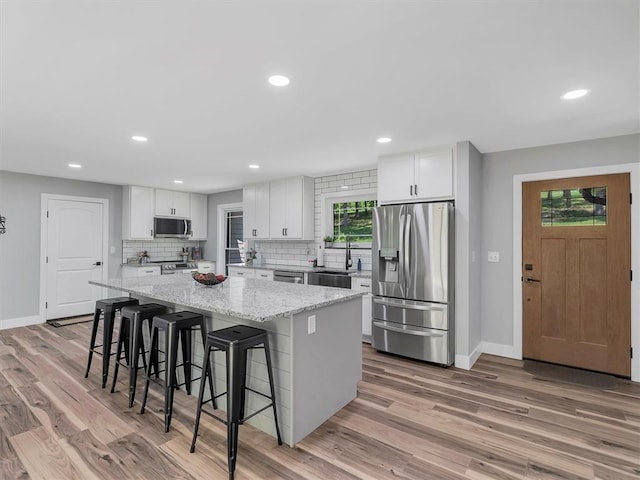 kitchen featuring stainless steel appliances, a kitchen island, light wood-style flooring, baseboards, and recessed lighting