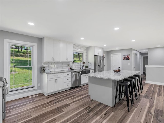 kitchen featuring appliances with stainless steel finishes, dark wood-type flooring, a kitchen breakfast bar, a center island, and white cabinetry