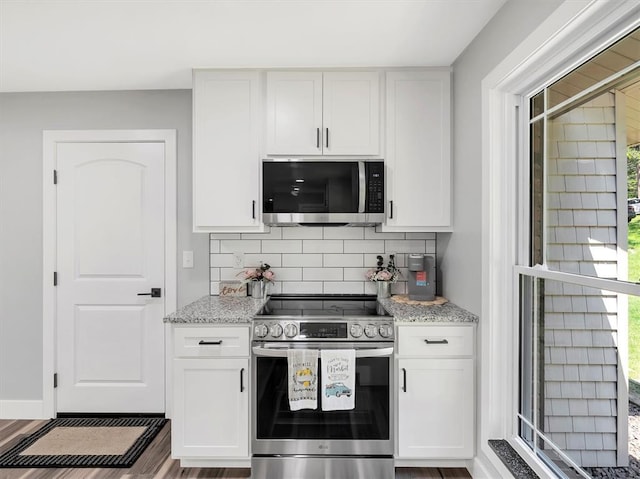 kitchen featuring appliances with stainless steel finishes, white cabinetry, tasteful backsplash, light stone countertops, and wood finished floors