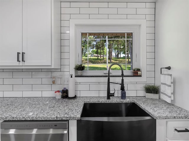 kitchen featuring a sink, stainless steel dishwasher, decorative backsplash, light stone countertops, and white cabinetry