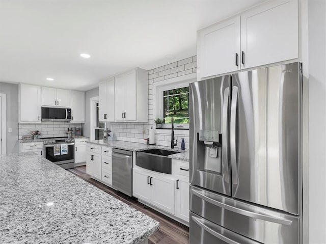 kitchen with stainless steel appliances, a sink, backsplash, dark wood-style flooring, and white cabinetry