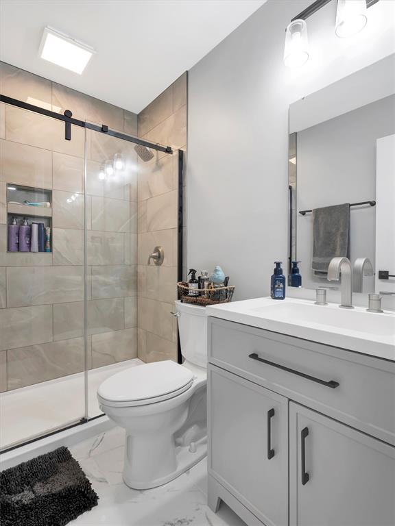 full bathroom featuring marble look tiles, a stall shower, toilet, and vanity