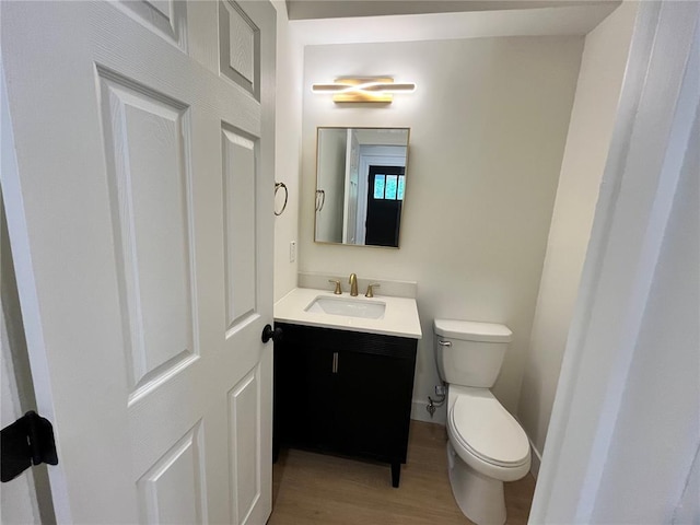 half bath featuring vanity, toilet, and wood finished floors