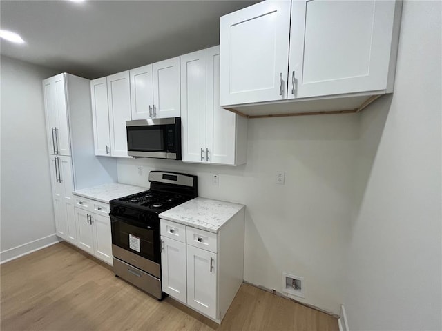 kitchen featuring appliances with stainless steel finishes, light wood-style floors, white cabinetry, and light stone countertops