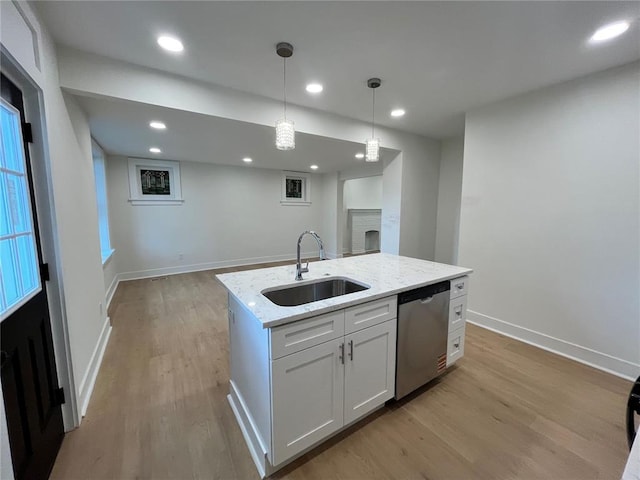 kitchen featuring a sink, dishwasher, light wood finished floors, light stone countertops, and pendant lighting