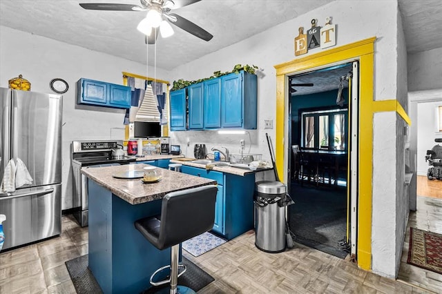 4615 San Francisco Ave, Saint Louis, MO 63115 - kitchen featuring appliances with stainless steel finishes, blue cabinets, wall chimney range hood, a ceiling fan, and a center island