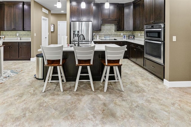 1514 Autumn St, Godfrey, IL 62035 - kitchen featuring stainless steel appliances, dark brown cabinetry, tasteful backsplash, an island with sink, and pendant lighting