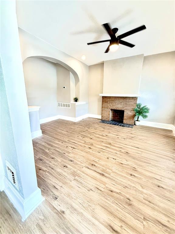 unfurnished living room featuring wood finished floors, a ceiling fan, baseboards, and a brick fireplace