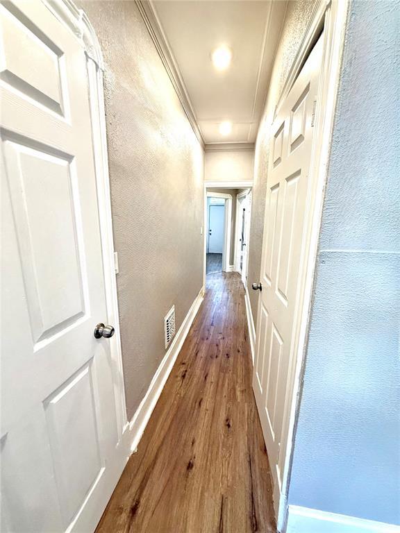 corridor with wood-type flooring, ornamental molding, baseboards, and a textured wall