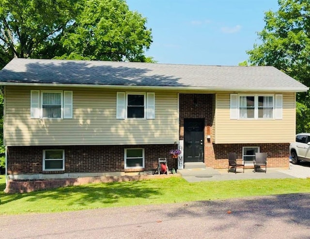 raised ranch featuring brick siding and a front lawn