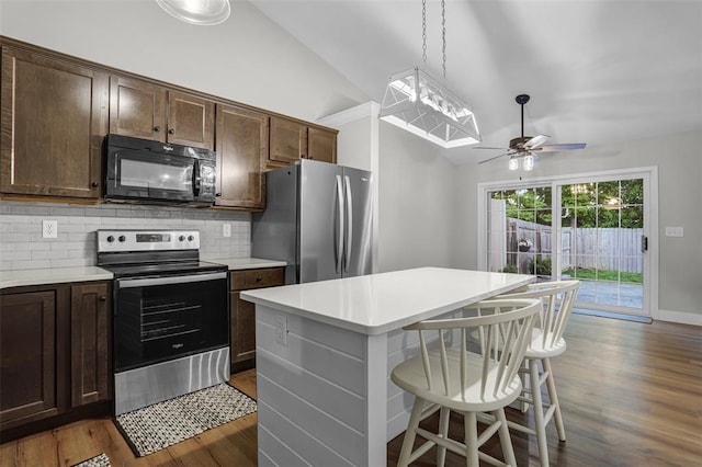 kitchen featuring stainless steel appliances, lofted ceiling, decorative backsplash, dark wood-type flooring, and light countertops
