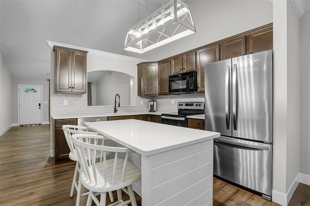 kitchen with stainless steel appliances, a kitchen island, backsplash, and dark brown cabinetry