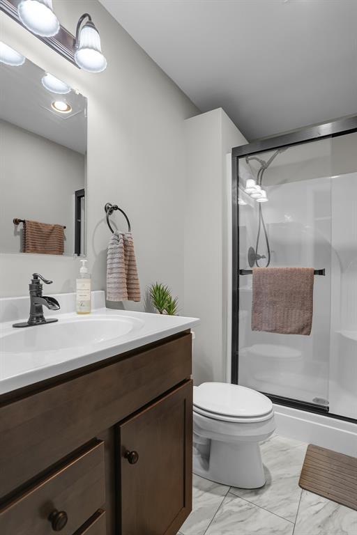 full bath with vanity, a shower stall, toilet, and marble finish floors