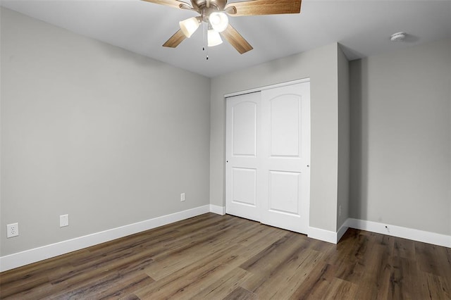 unfurnished bedroom featuring baseboards, dark wood-style floors, a closet, and a ceiling fan