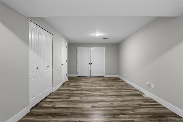 unfurnished bedroom with dark wood finished floors, baseboards, and two closets