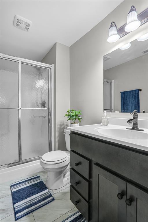 bathroom featuring a shower stall, marble look tiles, vanity, and toilet