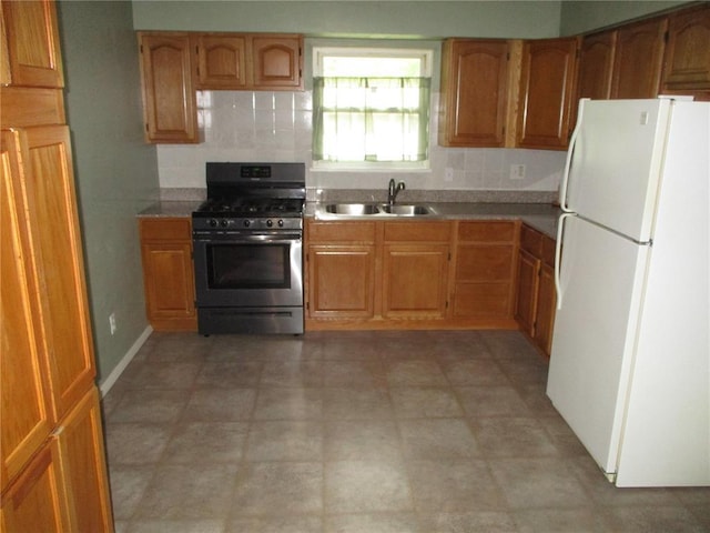 kitchen featuring freestanding refrigerator, stainless steel gas range oven, a sink, decorative backsplash, and brown cabinetry