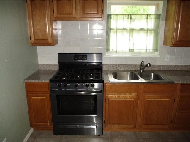 kitchen featuring gas range, a sink, decorative backsplash, and brown cabinets