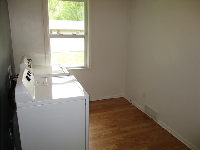 clothes washing area with washing machine and dryer, wood finished floors, and baseboards