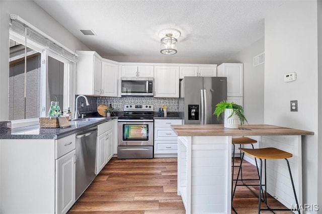 193 Harbor View Dr, Lake St Louis, MO 63367 - kitchen with appliances with stainless steel finishes, a kitchen breakfast bar, white cabinets, wood finished floors, and decorative backsplash