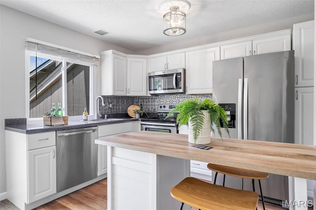 193 Harbor View Dr, Lake St Louis, MO 63367 - kitchen featuring appliances with stainless steel finishes, white cabinets, tasteful backsplash, light wood-style floors, and a breakfast bar area