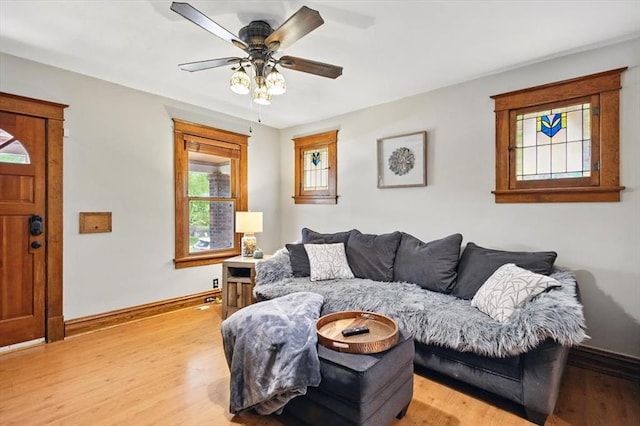 living area with baseboards, light wood-type flooring, and a ceiling fan