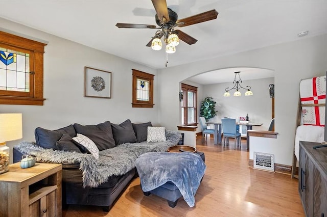living room with arched walkways, light wood-type flooring, a ceiling fan, and baseboards