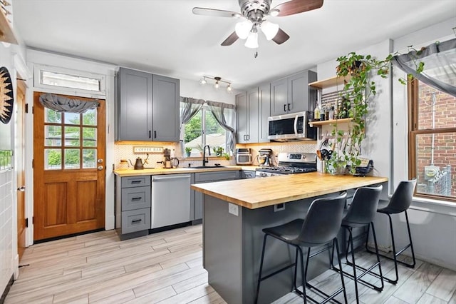 kitchen with stainless steel appliances, butcher block counters, a sink, open shelves, and gray cabinetry