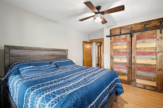 bedroom featuring a barn door, light wood-type flooring, and a ceiling fan