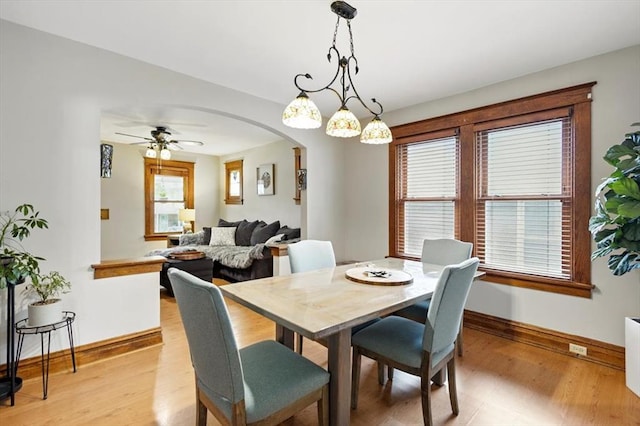 dining area with baseboards, arched walkways, light wood finished floors, and ceiling fan
