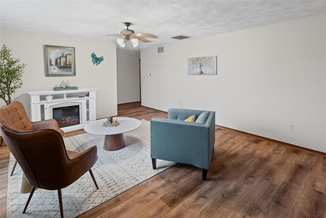 living area with wood finished floors, a ceiling fan, baseboards, and a glass covered fireplace