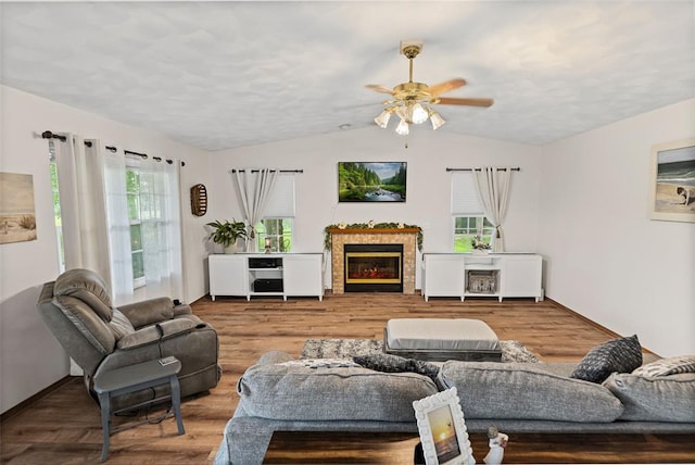 living room with lofted ceiling, a glass covered fireplace, ceiling fan, wood finished floors, and baseboards