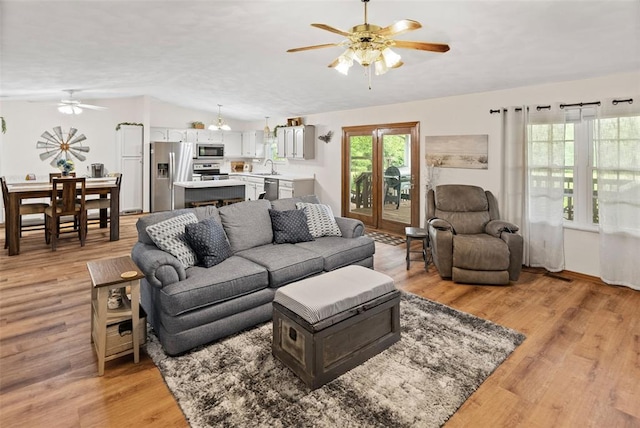 living area with a ceiling fan, light wood-type flooring, and vaulted ceiling
