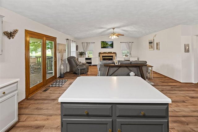 kitchen with gray cabinetry, lofted ceiling, ceiling fan, a lit fireplace, and wood finished floors