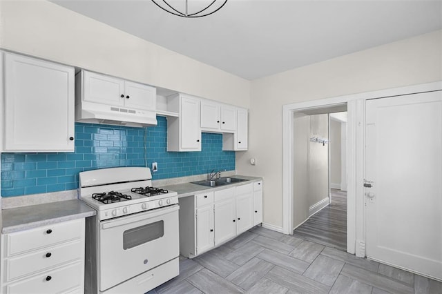 kitchen with white gas stove, under cabinet range hood, a sink, and white cabinetry